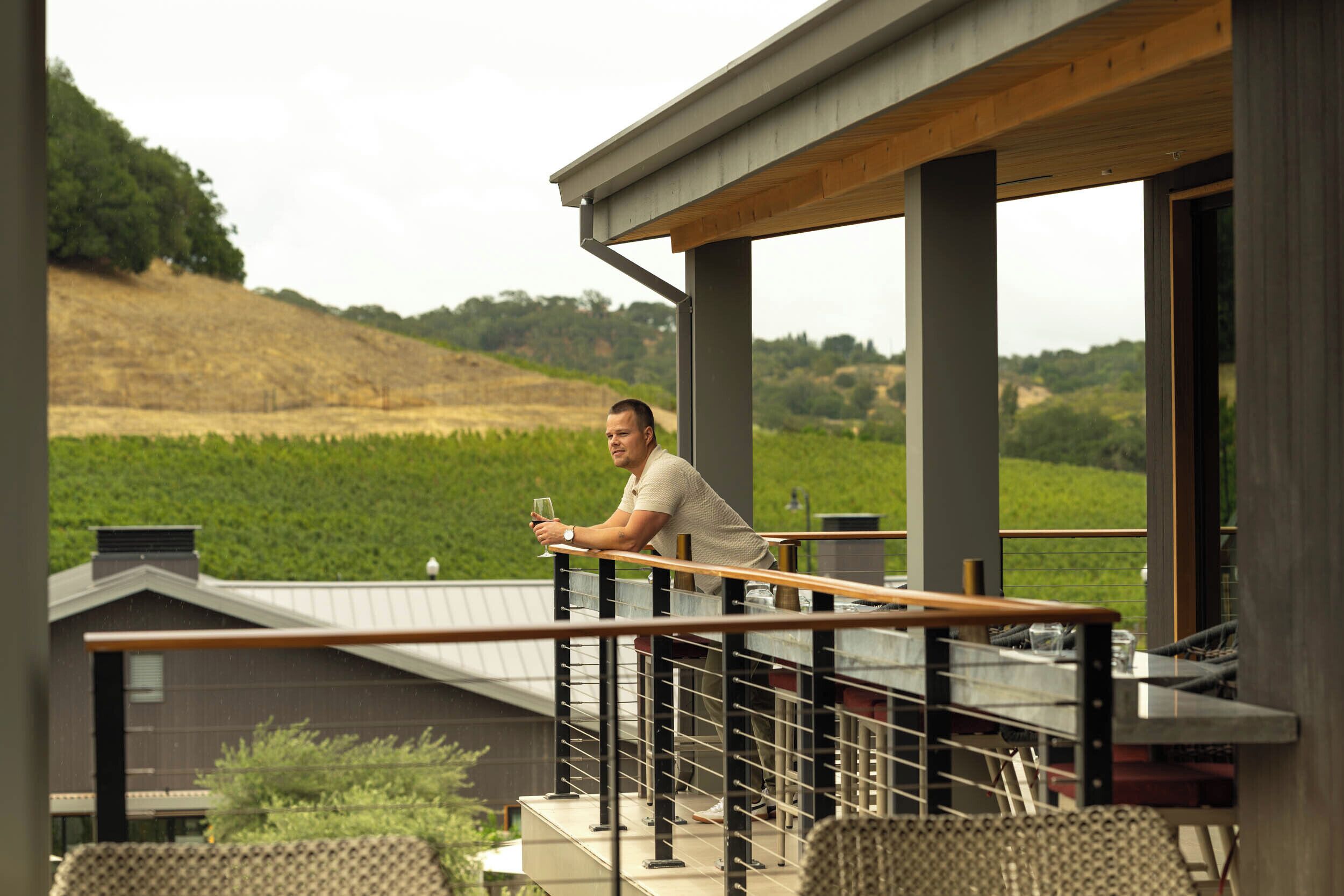 A man on a balcony with a view of a vineyard.