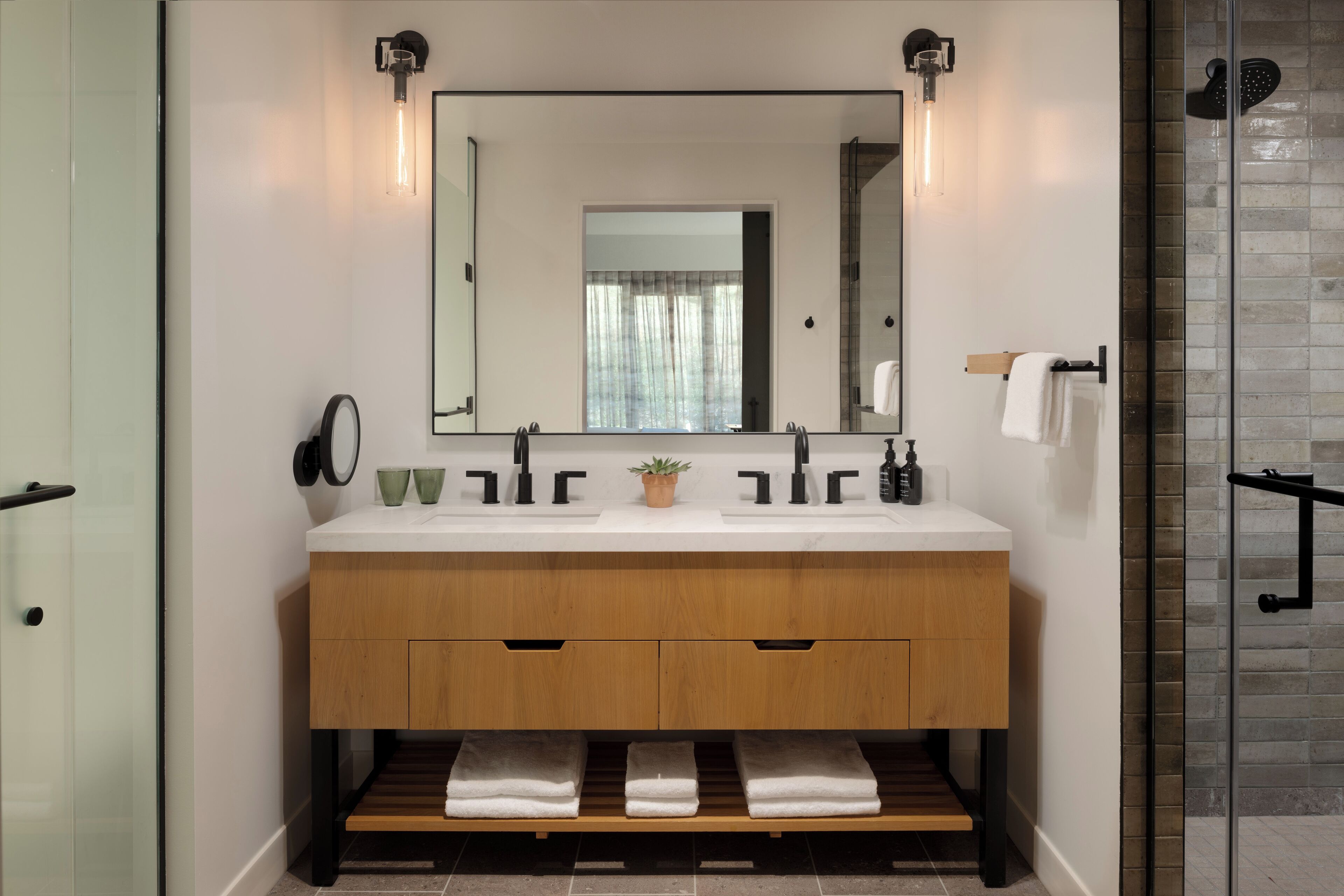 Un baño moderno con tocador de madera, dos lavamanos, un espejo grande y una cabina de ducha de vidrio.
