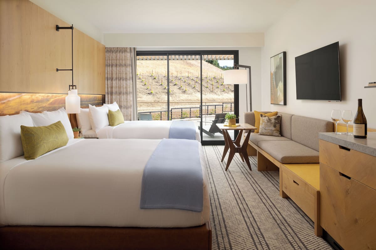 A hotel room with two beds, a sofa, a dining table, and a TV.