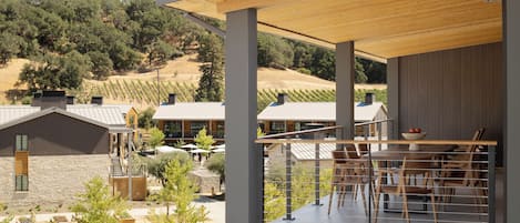 Un patio moderno al aire libre con techo de madera, zona de comedor con sillas y una mesa, y vistas a viñedos al fondo.