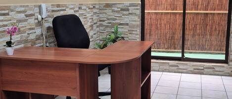 A conference room with a wooden desk, a black office chair, a potted plant, and a bamboo screen.