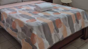 A neatly made bed with a patterned bedspread, a bedside lamp, and a window with curtains.