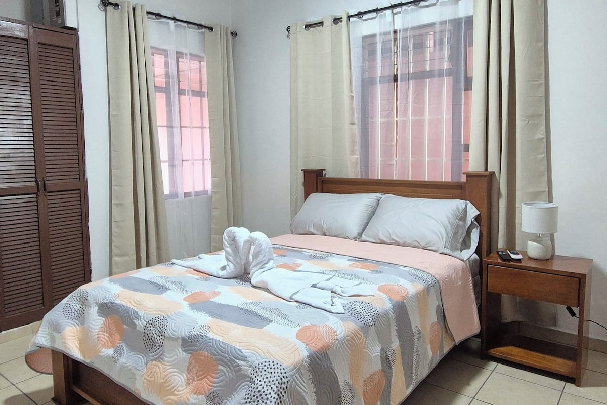 A neatly made bed with a patterned bedspread, a bedside table with a lamp, and an air conditioning unit on the wall.