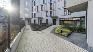 A modern building with a courtyard, paved walkways, and a fenced area with plants. - Sunny Apartment with Balcony | Parking | Close to Park (Wrocław)