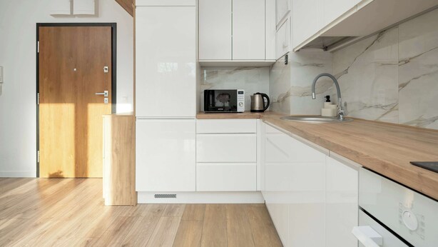 A modern kitchen with white cabinets, a wooden countertop, a microwave, a coffee maker, and a sink. - Sunny Apartment with Balcony | Parking | Close to Park (Wrocław)