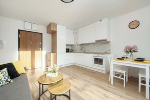 A modern kitchen with white cabinets, a wooden door, and a dining area with a white table and chairs.