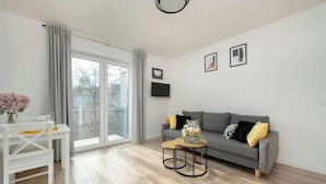 A modern living room with a grey sofa, a small round table, a white dining table, and a large sliding glass door leading to a balcony. - Sunny Apartment with Balcony | Parking | Close to Park (Wrocław)