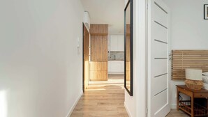 A hallway with wooden flooring, a wardrobe, a bedside table with a lamp, and a mirror. - Sunny Apartment with Balcony | Parking | Close to Park (Wrocław)