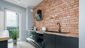 A modern kitchen with a brick wall backsplash, a built-in oven, and a window with blinds.