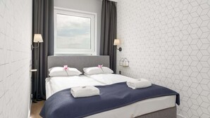 A modern hotel room with a large bed, two bedside lamps, a window with curtains, and a geometric-patterned wall.