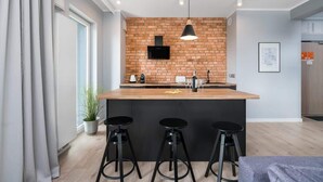 A modern kitchen with a brick backsplash, a wooden island with bar stools, and a black pendant light.