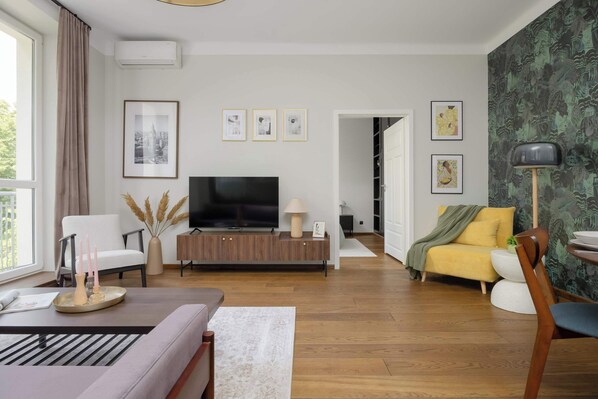Una sala de estar moderna con un televisor de pantalla plana, un sofá, una silla y un comedor con mesa y sillas.