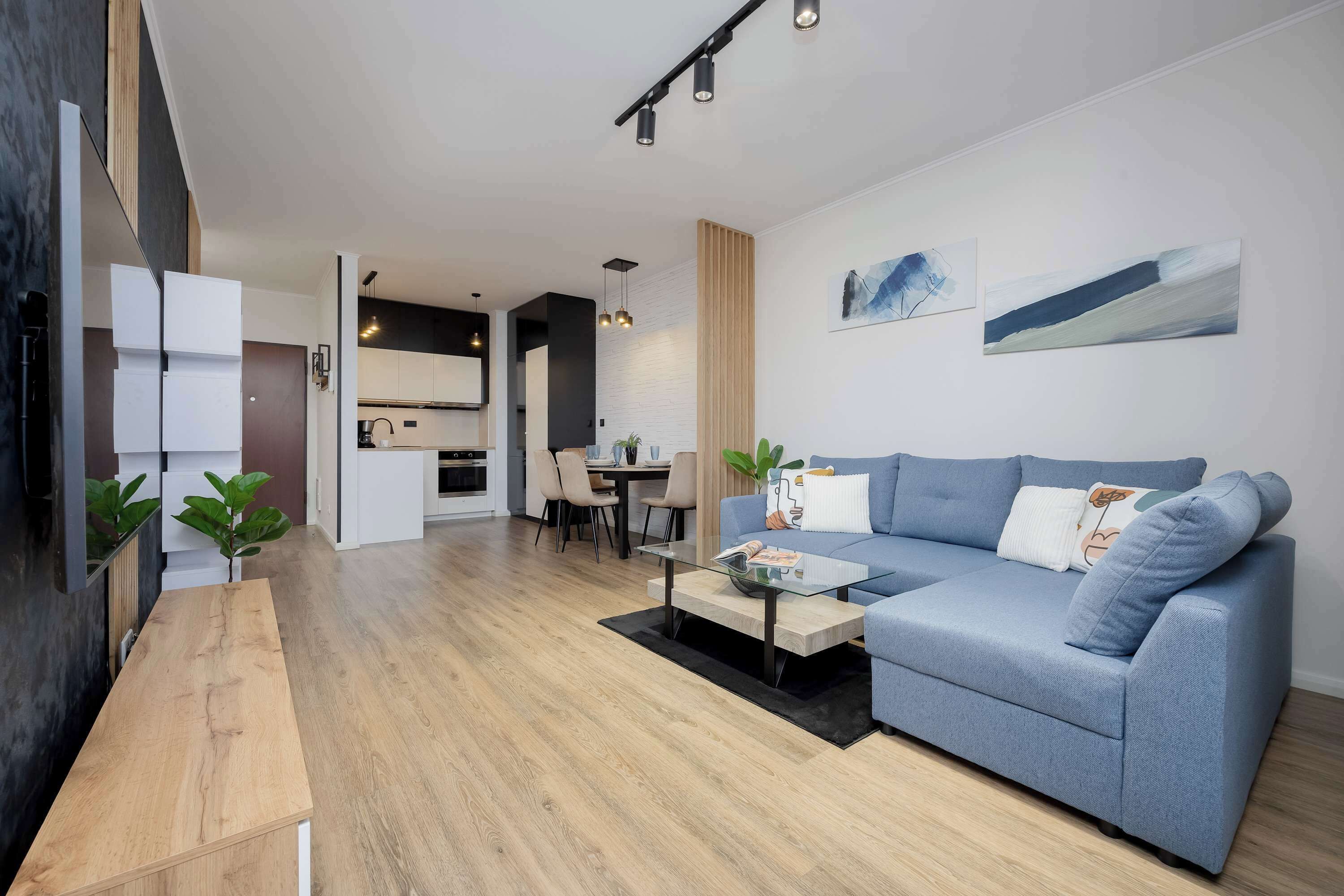Ein modernes Wohnzimmer mit einem blauen Sofa, einem Holztisch und einer Küche im Hintergrund.