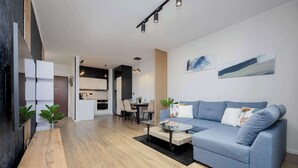 Un salon moderne avec un canapé bleu, une table basse en bois et une cuisine en arrière-plan.