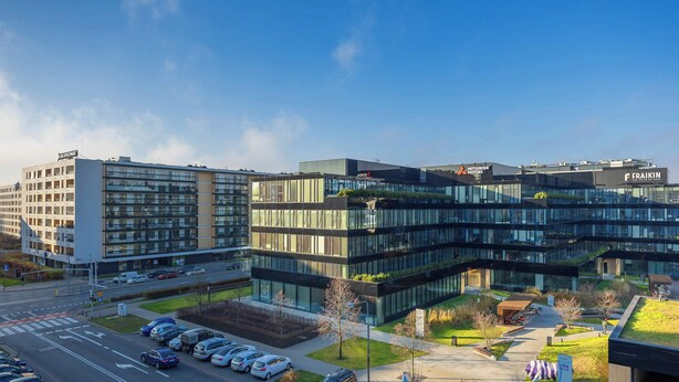 Un ensemble immobilier moderne comprenant plusieurs étages de bureaux, un espace de stationnement et une cour aménagée.
