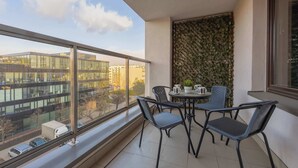 Un balcon donnant sur des immeubles, une table avec des chaises et un mur décoratif.