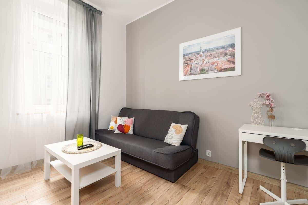 A bright living room with a gray sofa, a white coffee table, and wooden flooring, complemented by natural light from the windows.

