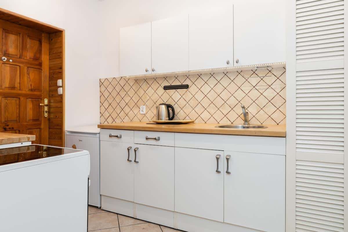 Una cocina con armarios blancos, encimera de madera, un hervidor y un lavabo.