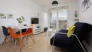 Una sala moderna con un sofá negro, sillas anaranjadas y negras, una mesa de comedor blanca y un televisor.