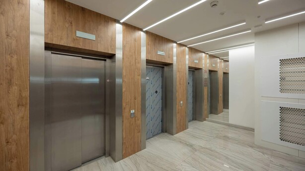 A modern elevator area with wooden paneling and a marble floor.