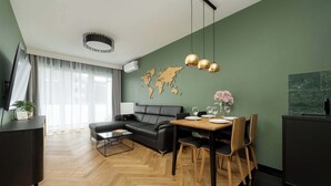 A modern living room with a herringbone floor, a black leather sofa, a dining table with chairs, and a world map on the wall.
