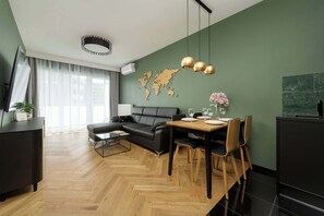 A modern living room with a herringbone floor, a black leather sofa, a dining table with chairs, and a world map on the wall.