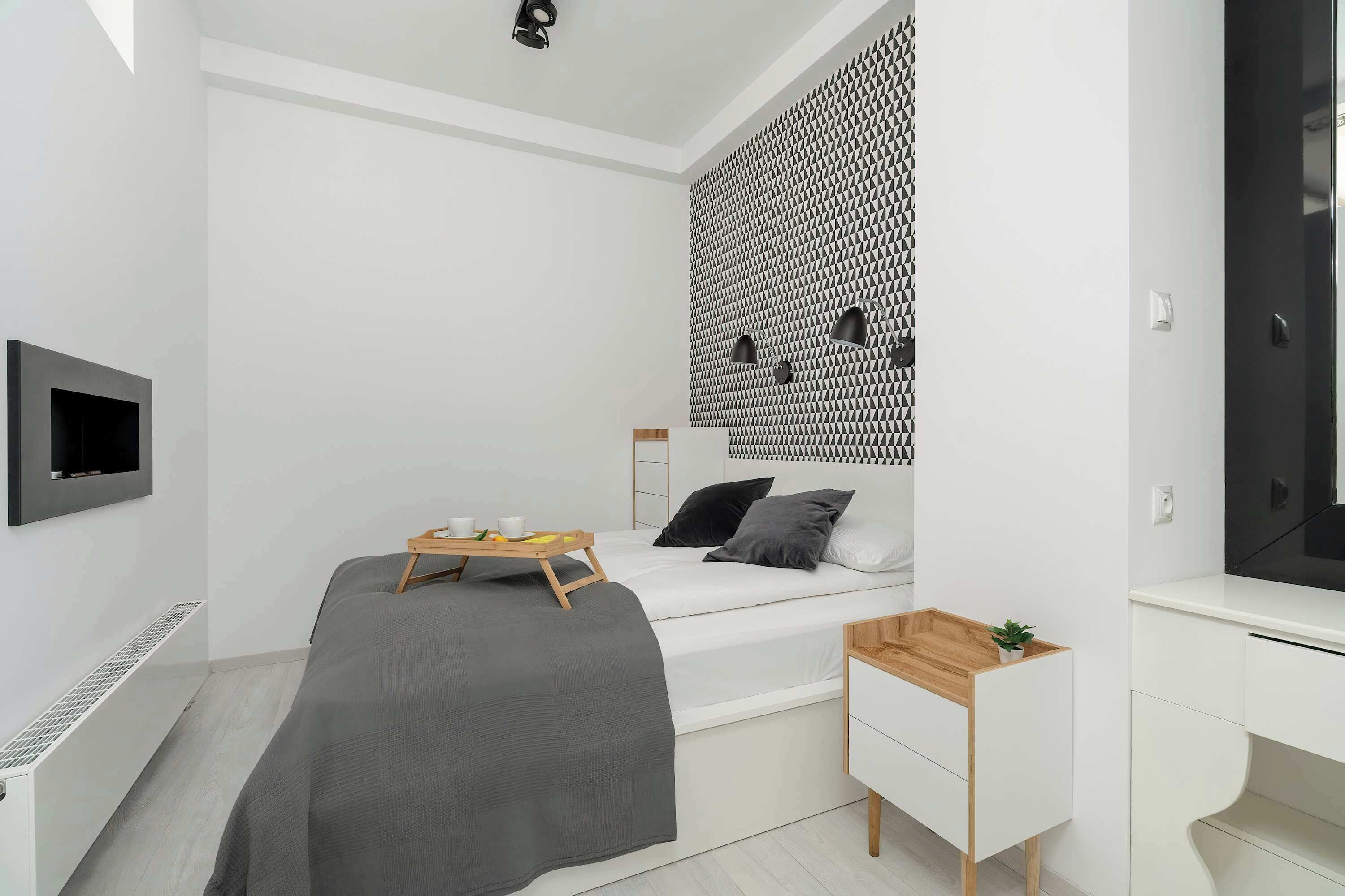 Un dormitorio moderno con cama, mesita de noche y televisor montado en la pared.