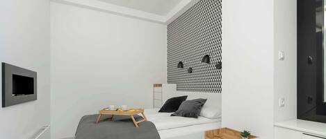 Un dormitorio moderno con cama, mesita de noche y televisor montado en la pared.