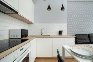 Cocina compacta con armarios blancos, microondas, cafetera y comedor con mesa y sillas.