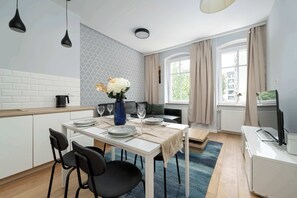 Una cocina moderna con armarios blancos, una mesa de comedor para cuatro personas y un ventanal con cortinas.