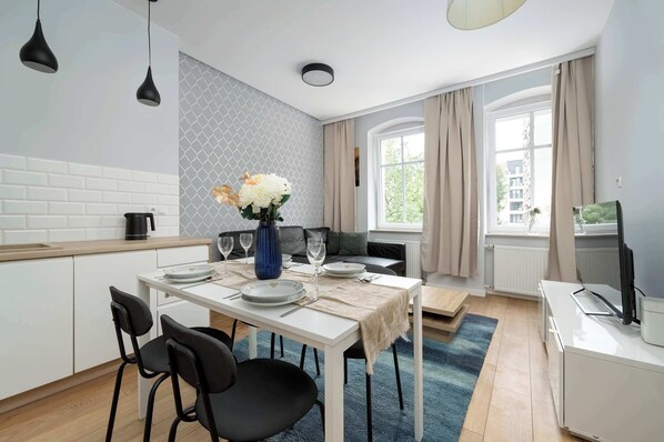 Una cocina moderna con armarios blancos, una mesa de comedor para cuatro personas y un ventanal con cortinas.