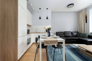 Una cocina moderna con armarios blancos, una mesa de comedor con sillas, un sofá de cuero negro y un papel tapiz estampado.