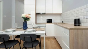 A modern kitchen with white cabinets, a microwave, a coffee maker, and a dining area with a table set for two.
