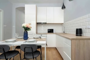 Una cocina moderna con armarios blancos, microondas, cafetera y un comedor con mesa dispuesta para dos.