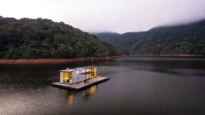Una casa flotante en un lago tranquilo rodeada de colinas boscosas.