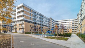 A multi-story residential building with balconies, a paved walkway, and a playground area.