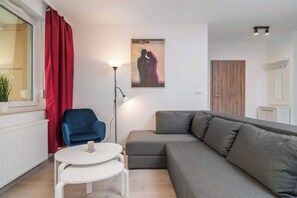 A modern living room with a grey sectional sofa, a blue chair, a white table, and a red curtain.