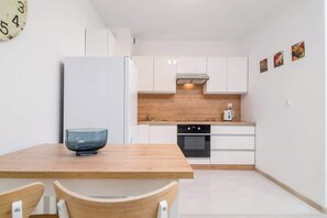 A compact kitchen with white cabinets, a wooden countertop, a built-in oven, and a single bowl on the table.