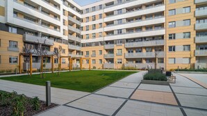 A multi-story residential building with balconies, a central courtyard, and a small garden area.