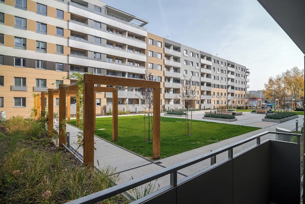 A multi-story residential building with balconies, a grassy courtyard, and a wooden pergola structure.