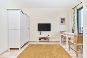 A room with a TV, a dining table, chairs, a sofa, and a wardrobe.