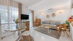 Ein modernes Wohnzimmer mit einem Glastisch, weißen Stühlen, einem beigen Sofa und einem Fernseher.