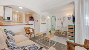 Ein modernes Wohnzimmer mit einer Couch, einem Couchtisch, einem Essbereich mit Tisch und Stühlen sowie einer Küchenzeile mit Kühlschrank und Mikrowelle.