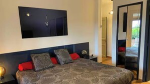 Une chambre moderne avec un grand lit, un téléviseur fixé au mur et une porte coulissante donnant sur un balcon.