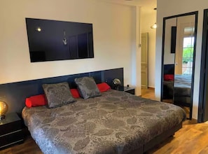 A modern bedroom with a large bed, a wall-mounted TV, and a sliding door leading to a balcony.