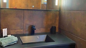 Une salle de bain moderne avec un plan de toilette foncé, un lavabo et un grand miroir.