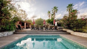 Une piscine entourée de verdure et de palmiers, avec des chaises longues et des parasols.