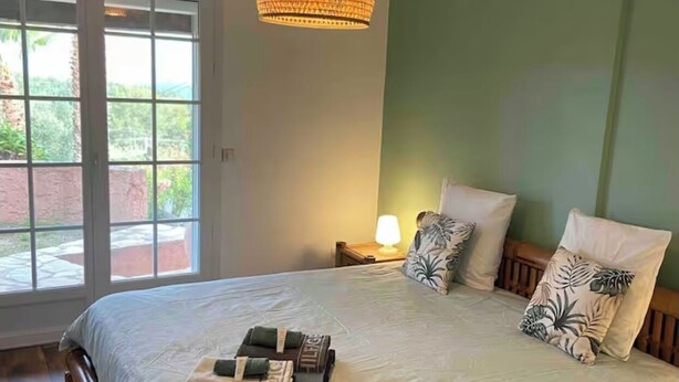 Une chambre avec un grand lit, une lampe suspendue, une table de chevet et une vue sur l’extérieur, visible à travers une porte vitrée.