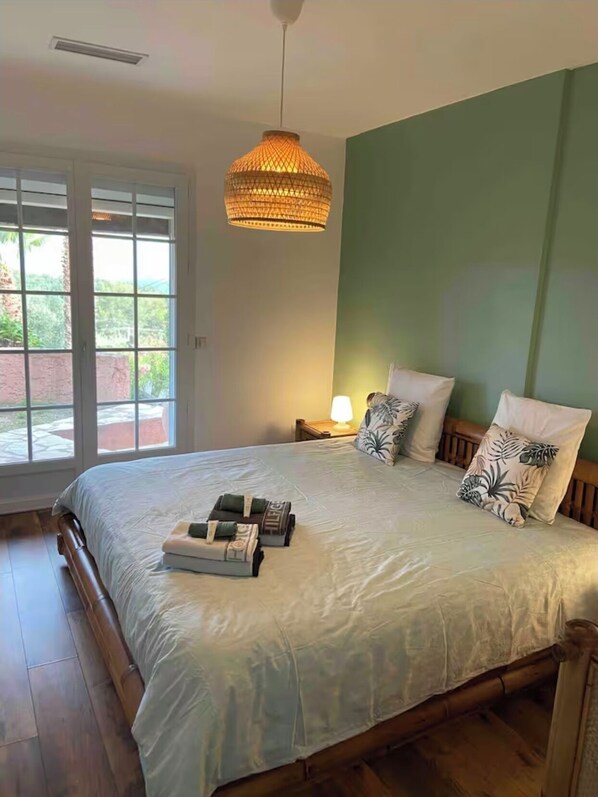 A bedroom with a large bed, a hanging lamp, a nightstand, and a view through a glass door.