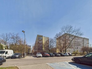 Een parkeerplaats met diverse auto's en een witte bestelwagen, omringd door gebouwen en kale bomen.